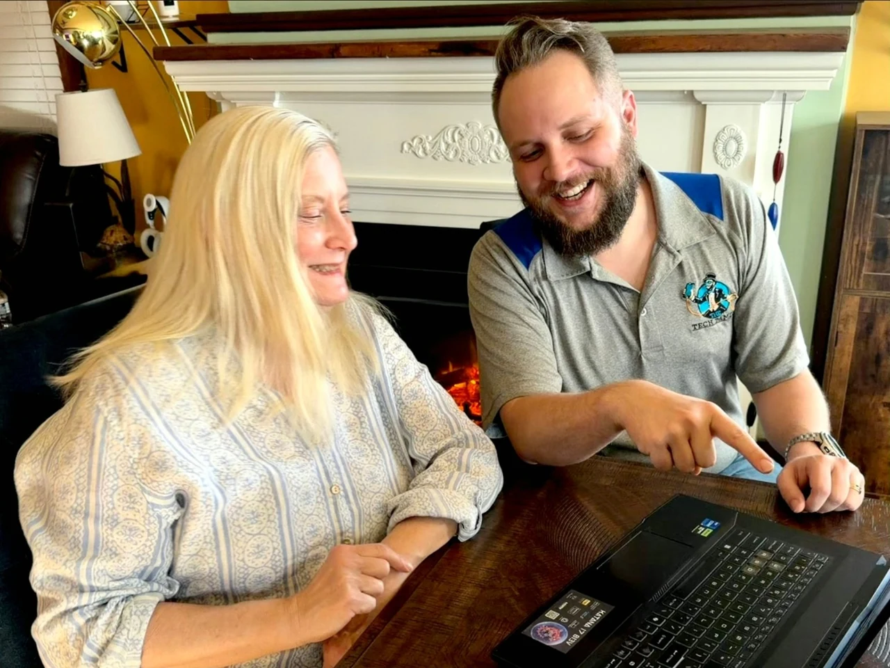 Josh smiling and helping a woman with her laptop at a kitchen table